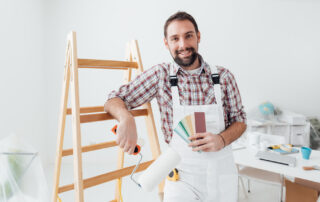 Confident professional painter posing, he is holding a paint roller and color swatches, home renovation and decoration concept
